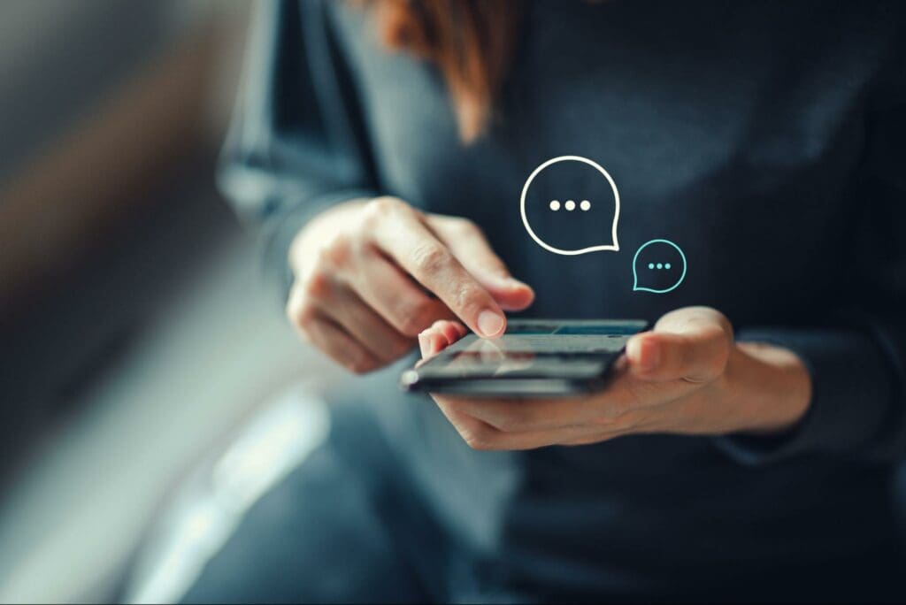 Close-up of a person's hands using a smartphone with digital chat bubbles appearing on the screen.